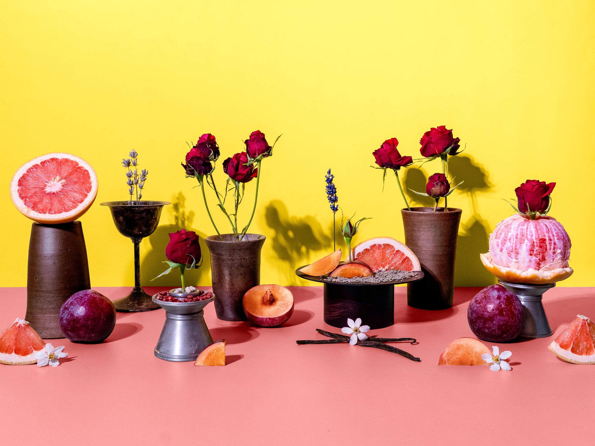 Decorative setup with flowers, fruits, and small tables against a yellow and pink background