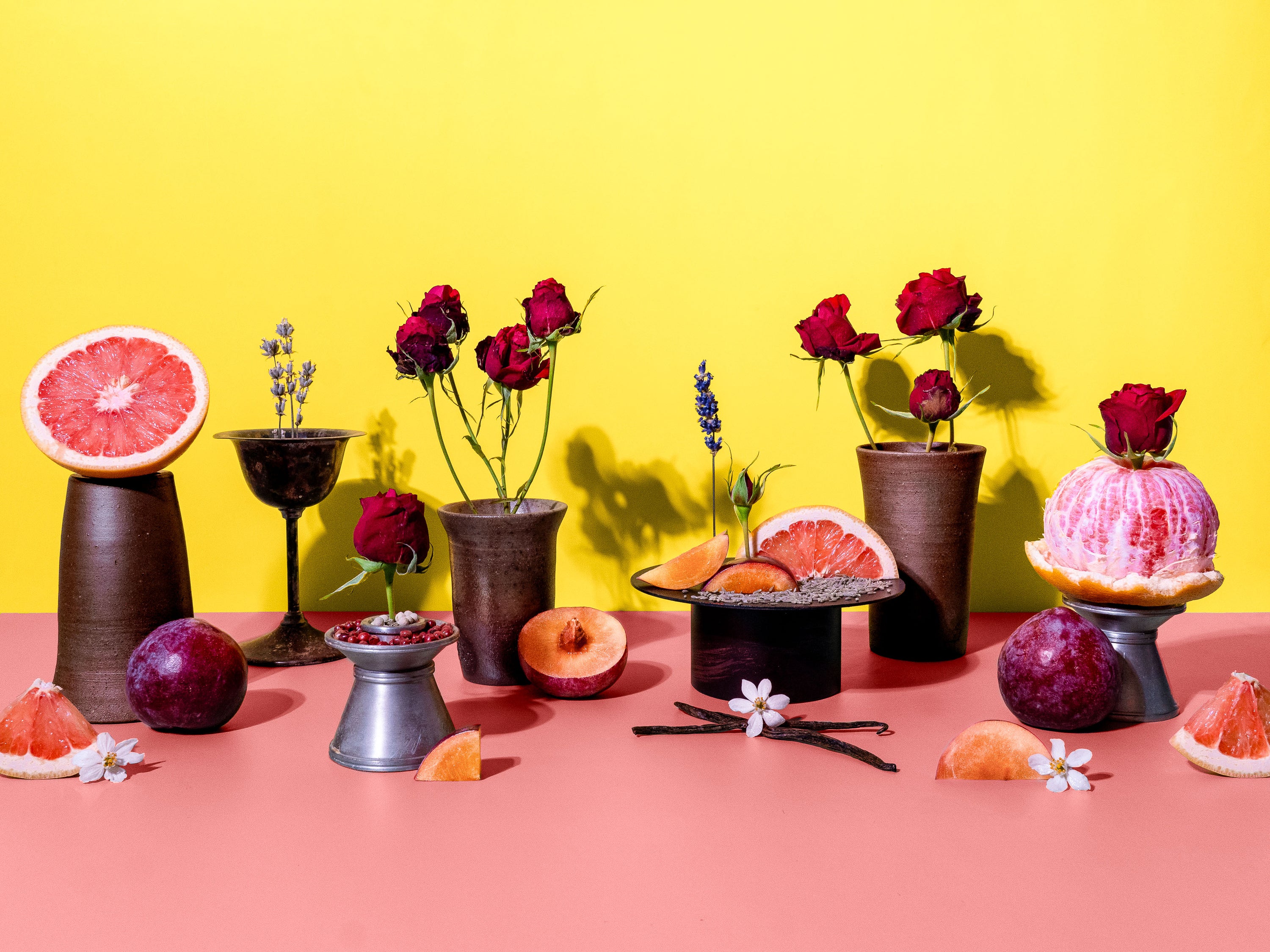 Decorative setup with flowers, fruits, and small tables against a yellow and pink background