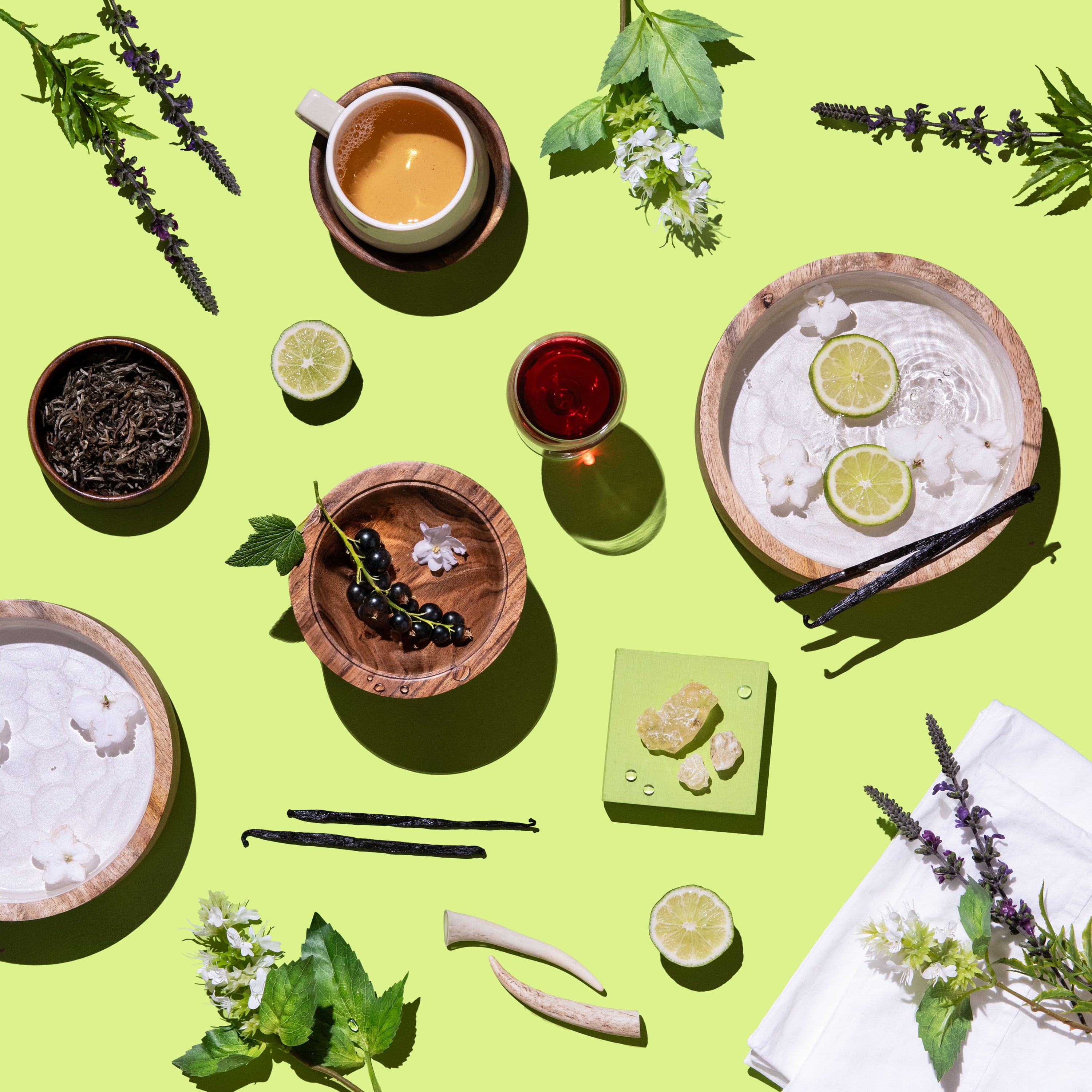 Table setting with wooden bowls, white tea, and limes on a green background