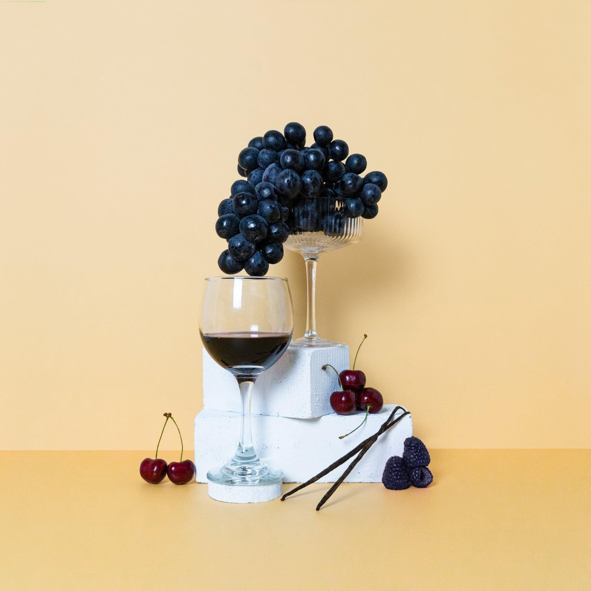 A composition featuring a glass of red wine, accompanied by cherries and grapes, against a yellow background.