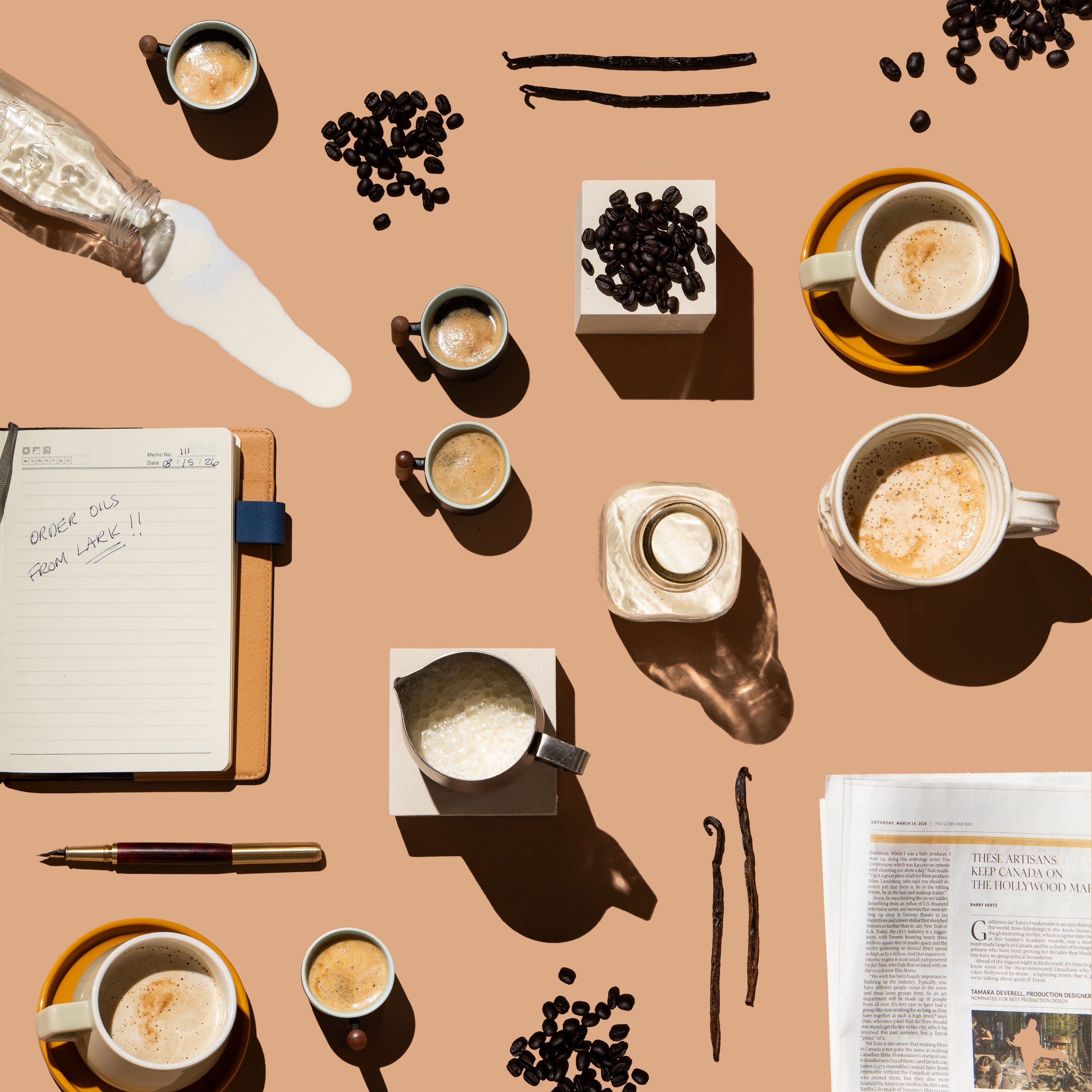 Coffee-themed flat lay with cups, beans, vanilla pods, and a notebook on a beige background