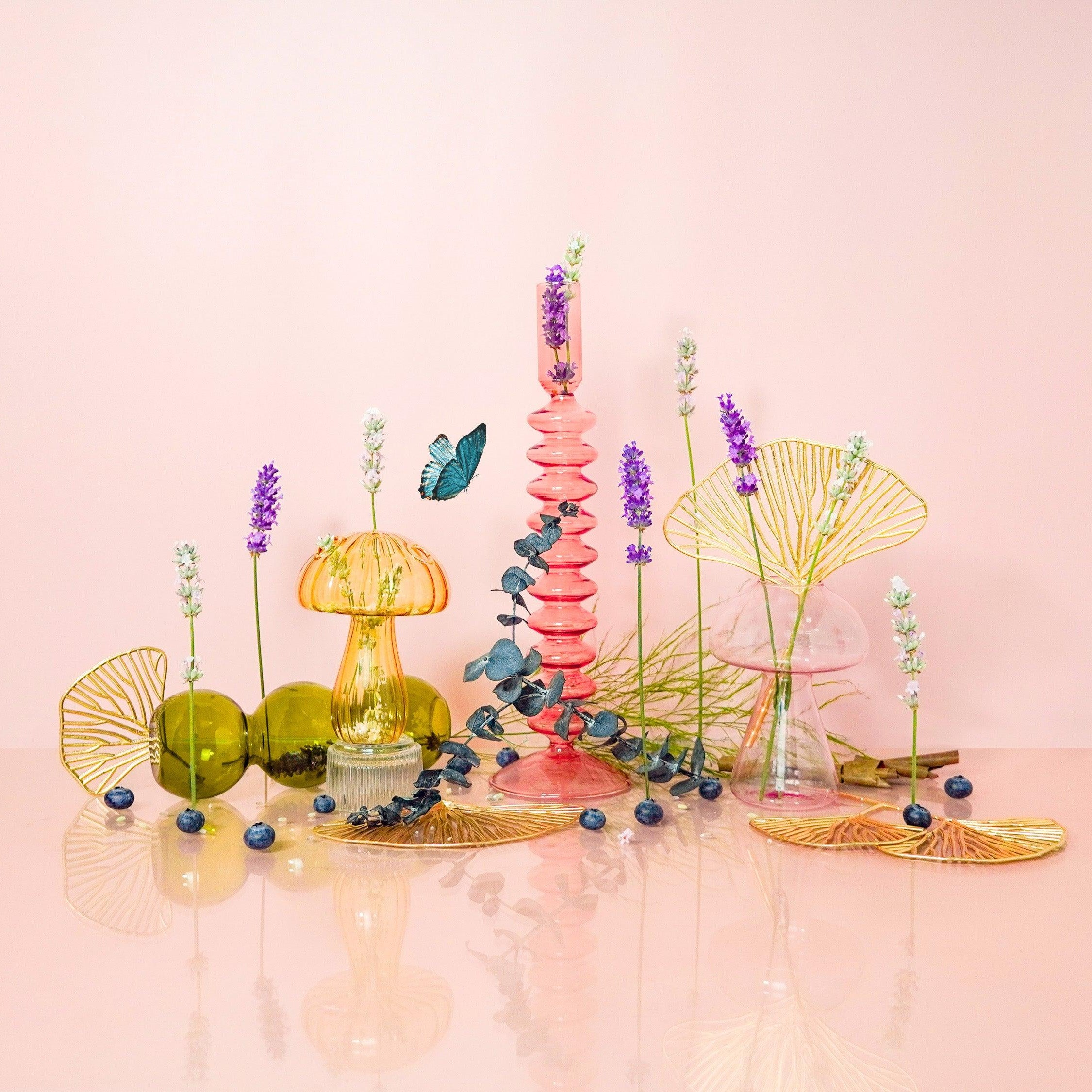 A still life arrangement featuring a variety of plant-like objects and scent bottles, with top notes of lavender and citrus, heart of berries and violets, and a base of sweet amber and menthol wood.