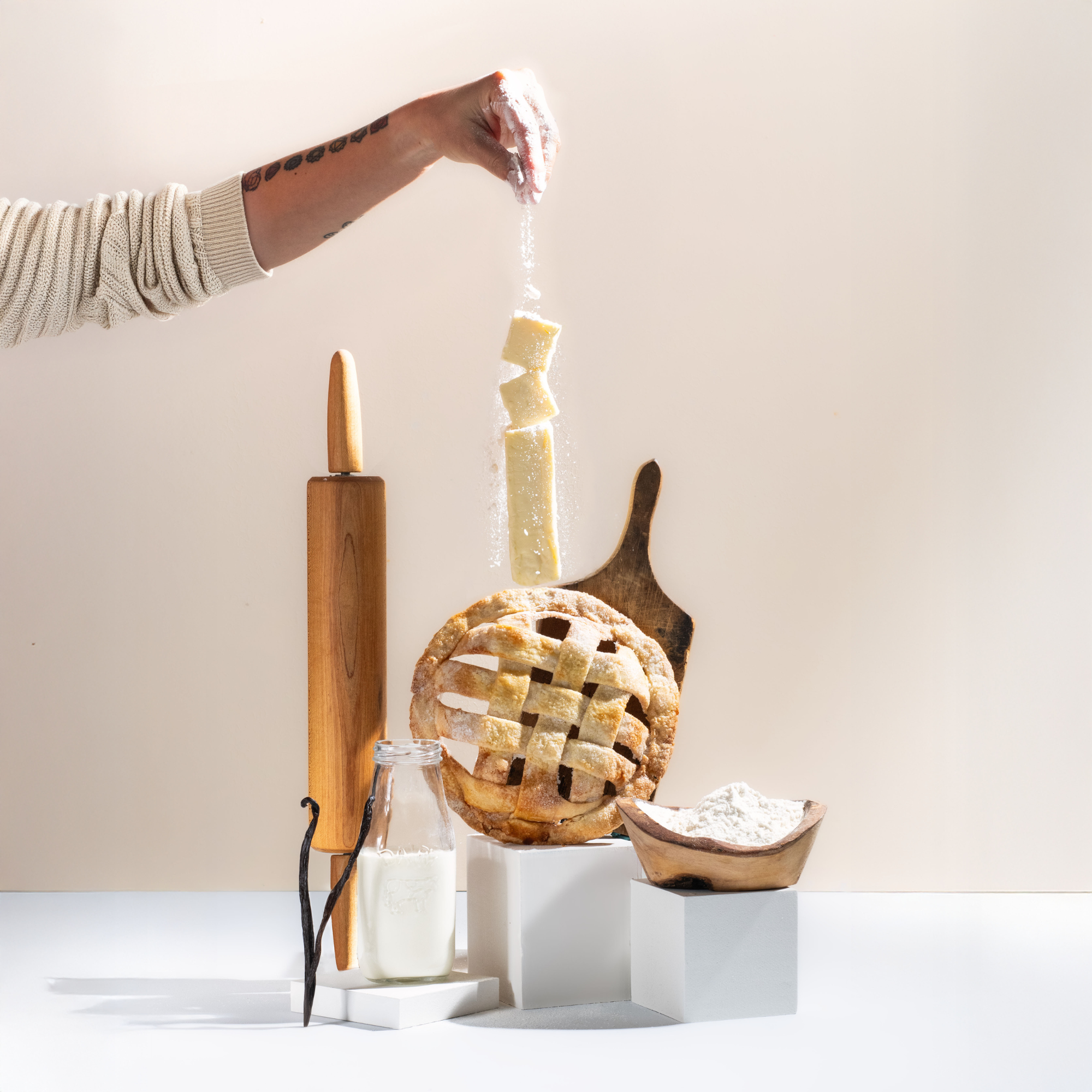 Pie crust being cut with a knife, surrounded by baking tools and ingredients on a white surface.