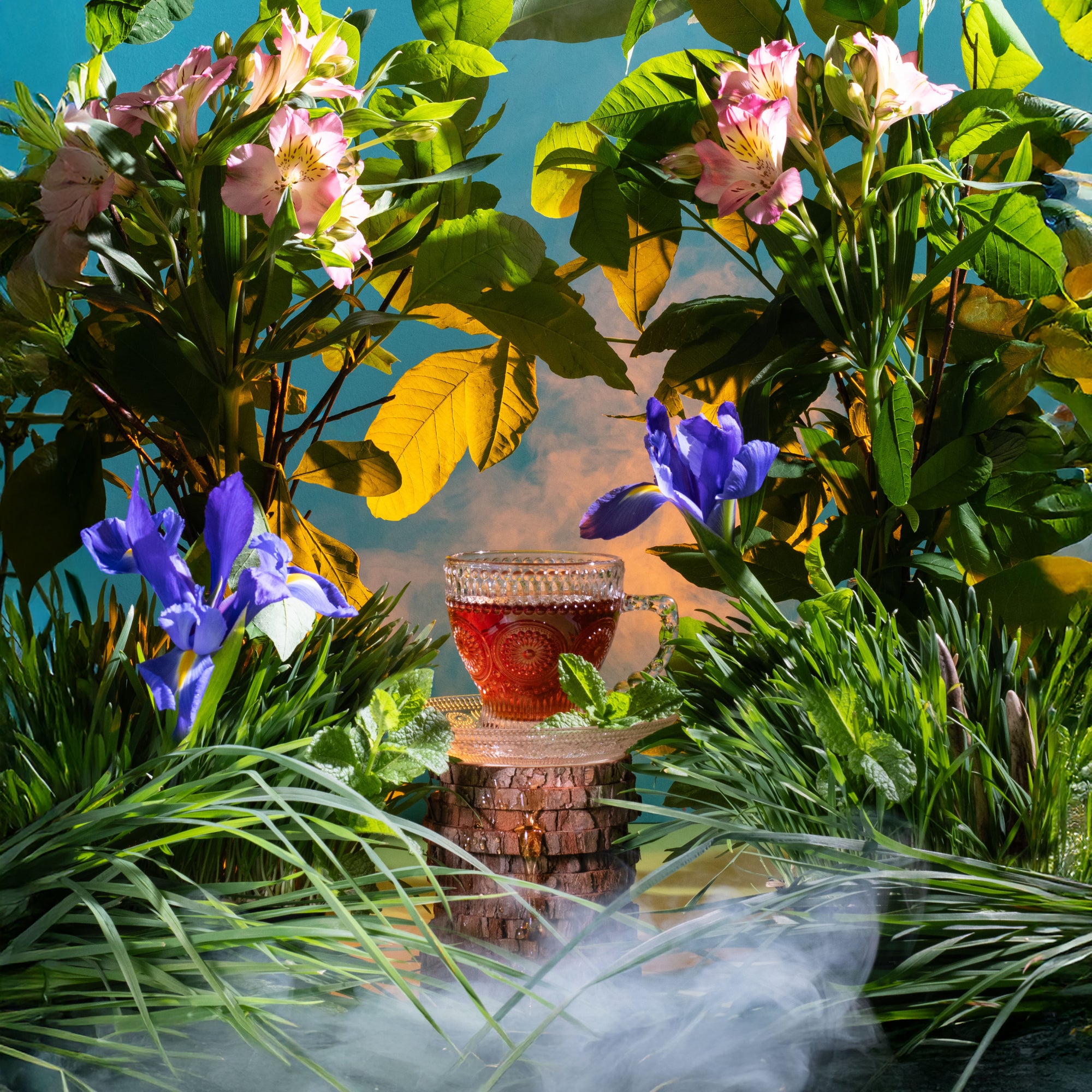 Teacup with red liquid surrounded by green foliage and flowers