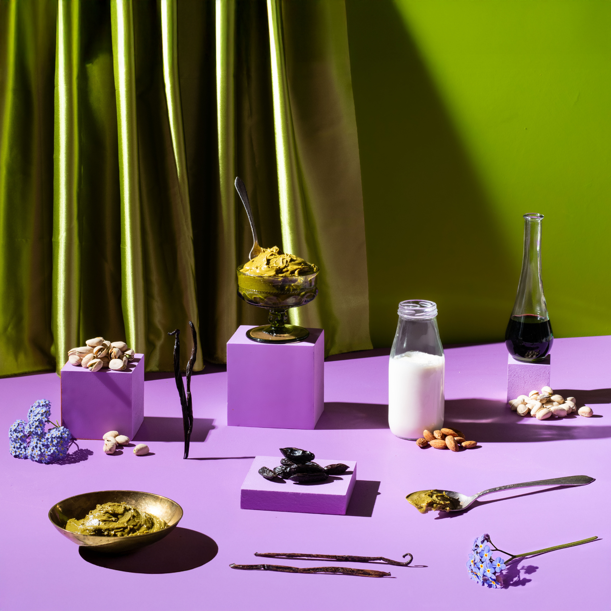 Tabletop setup with various items including a bottle, bowls, and a spoon against a green curtain and purple surface.