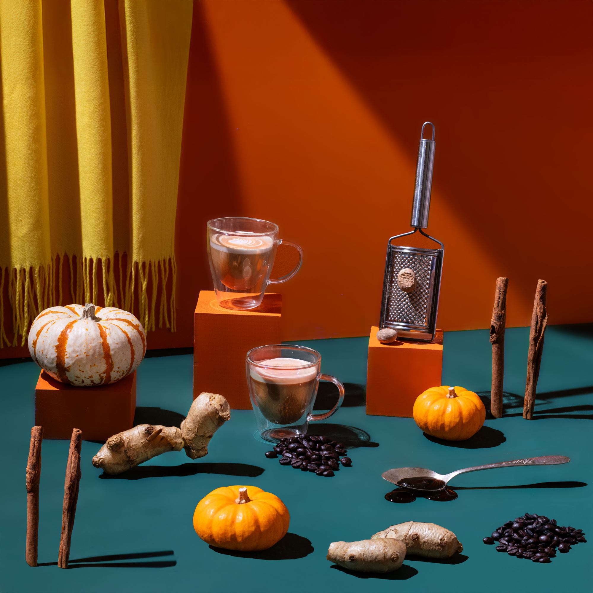 Spice rack, coffee cups, pumpkins, and ginger on a teal surface with an orange wall and yellow curtain.