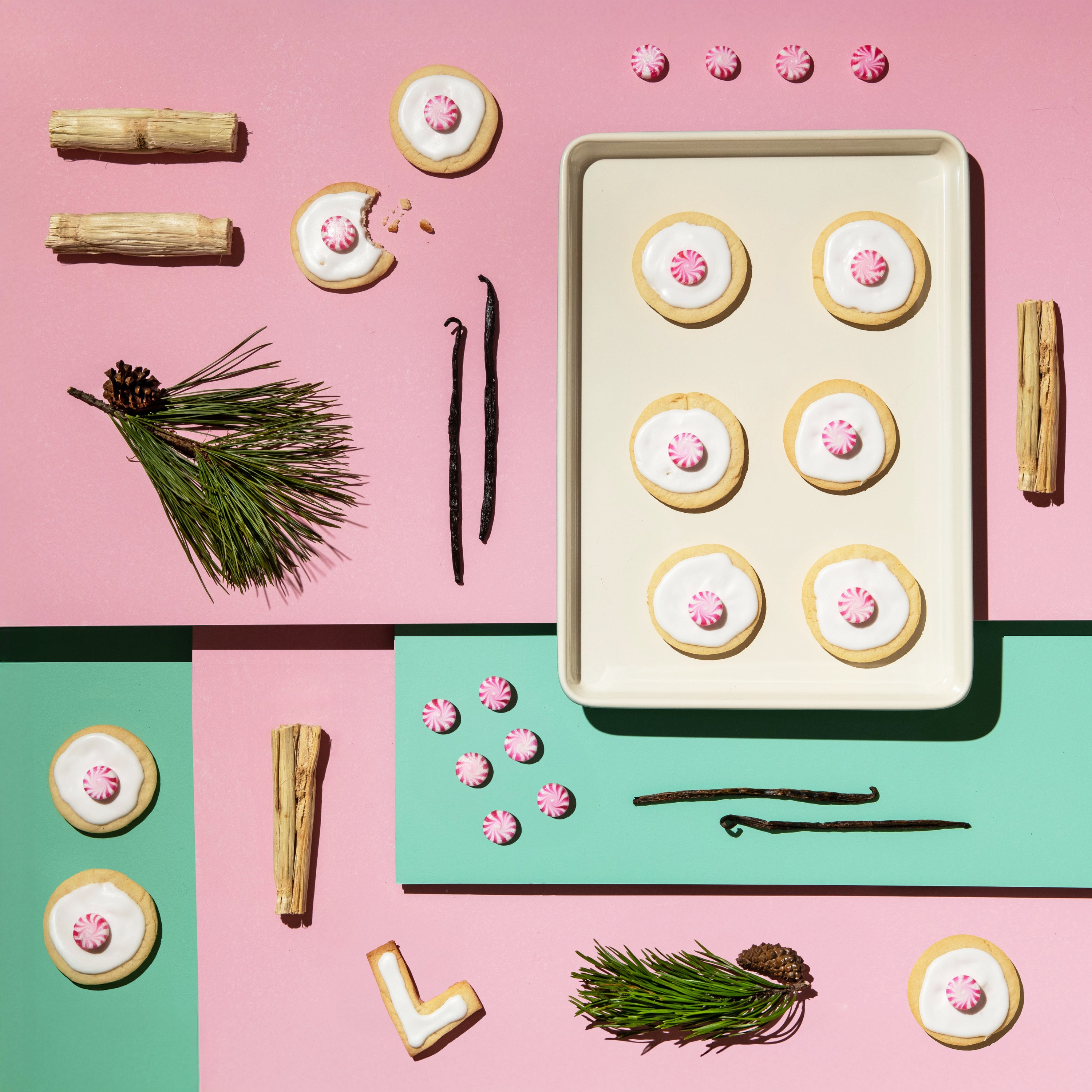 Decorative cookies with pink centers on a baking tray, surrounded by cinnamon sticks, vanilla beans, and pine branches on a pink and green background.