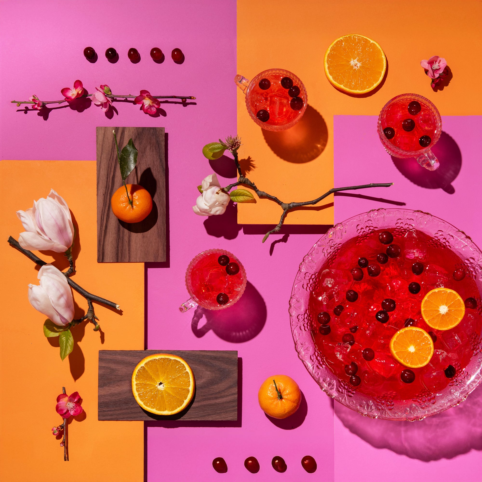 Colorful arrangement of drinks, fruits, and flowers on a pink and orange background