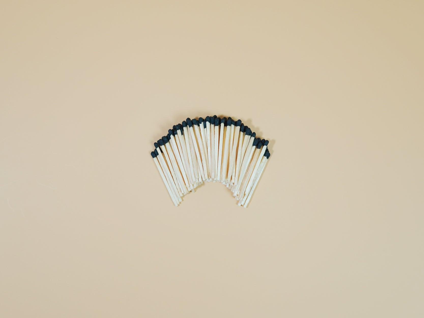 A collection of black matchsticks fanned out on a beige background